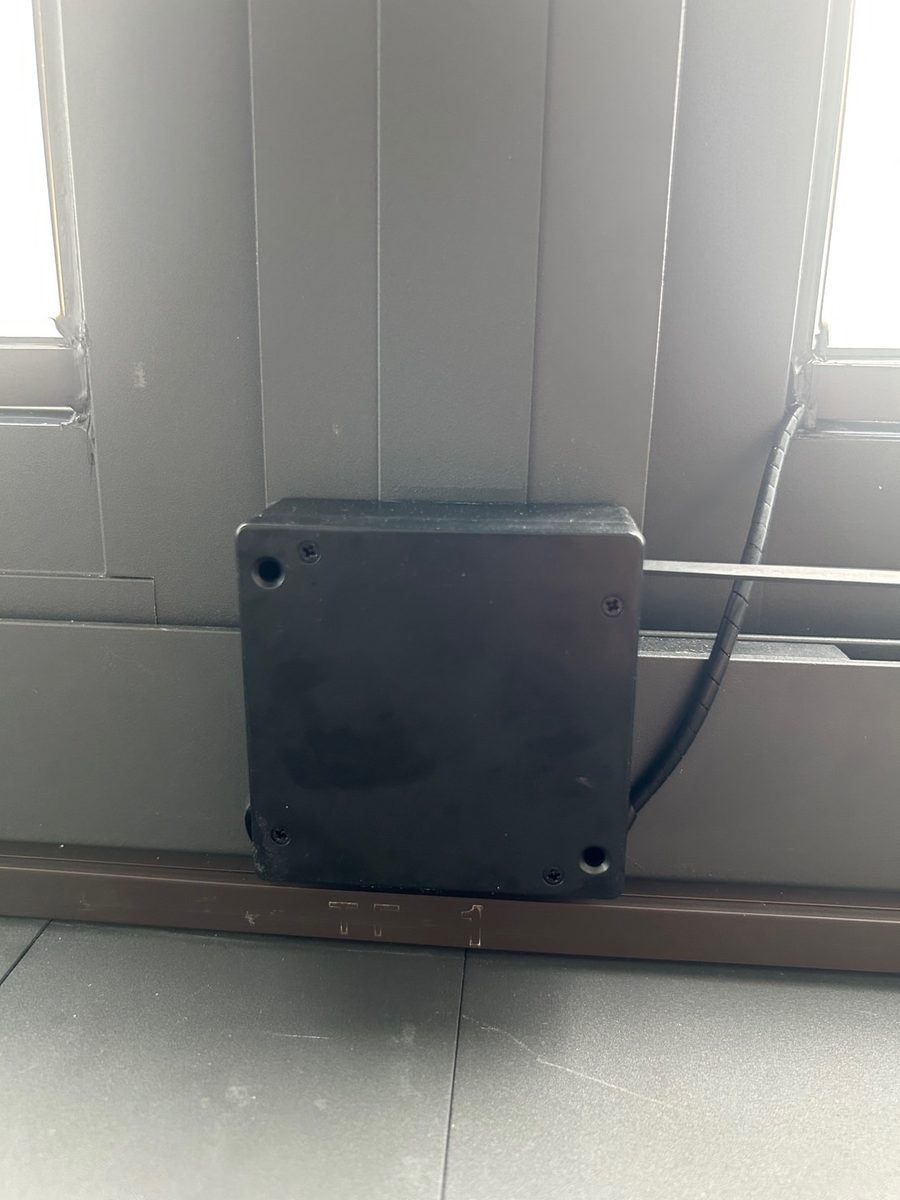 黑色伸縮電線盒外掛在鋁窗下軌旁，捲線沿軌道向右延伸